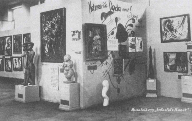 Vista de la exposición Arte degenerado, Múnich, 1937, sala 3, planta superior (conocida comola «pared dadá») con obras de George Grosz, Kurt Schwitters, Vasily Kandinsky (pintura mural), Paul Klee,Raoul Hausmann, Lyonel Feininger y esculturas de Ernst Ludwig Kirchner, Christoph Voll, Rudolph Haizmann,Oswald Herzog y Margarethe Moll